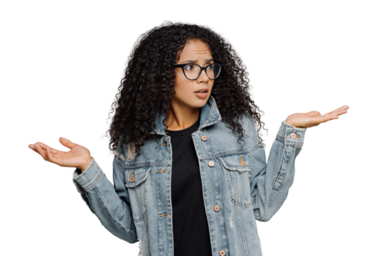 Confused unaware Afro woman with crisp hair, raises hands in bewilderment, looks aside, cannot make decision, wears spectacles and jean jacket, isolated over grey background. What should I do now?