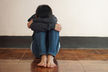 Depressed unidentified boy sits alone on the floor, feeling sad and cry, hug his knee. Concept :...