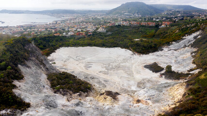 Aerial view of Solfatara of Pozzuoli, near Naples, Italy. It is a dormant volcano and part of the Phlegraean Fields volcanic area. In background there are Pozzuoli town and Mediterranean sea. - obrazy, fototapety, plakaty