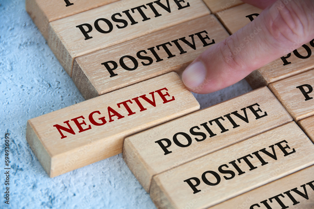Wall mural finger pushing negative text on wooden block from the rest of the wooden blocks with positive text. 