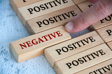 Finger pushing negative text on wooden block from the rest of the wooden blocks with positive text....