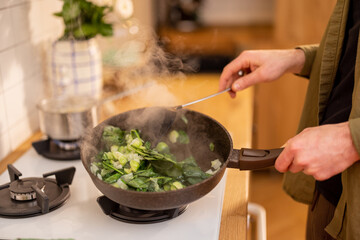Man frying spinach leaves and brussels sprouts in cooking pan, close-up