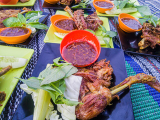 serving of fried chicken thighs on a plate with dipping hot chili sauce, and sliced ​​cucumber and cabbage leaves as fresh vegetables and basil leaves as seasoning