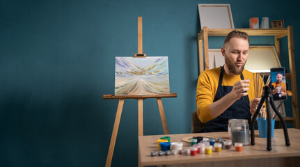 Young artist man sitting at desk and recording online art class at art studio. Blogger making a...