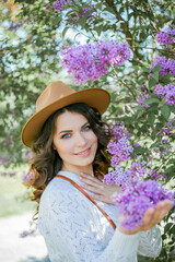 Portrait of beautiful young dark-haired woman with blue eyes in hat near the blooming. Happy model with curly hair. Spring.