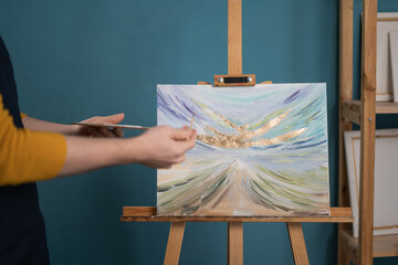 Male artist giving the last touches of paint to the new painting doing on his home workshop....