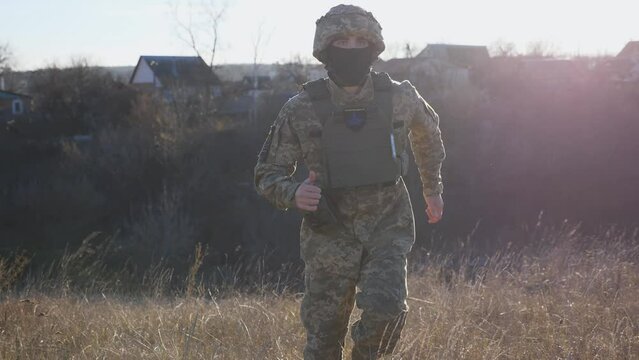 Young male military in uniform jogging among dry grass at countryside. Ukrainian army soldier running through uncultivated meadow at sunny day. Invasion resistance. War between russia and Ukraine