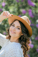 Portrait of beautiful young dark-haired woman with blue eyes in hat near the blooming. Happy model with curly hair. Spring.