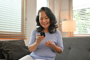 Happy senior woman checking blood sugar level by digital glucose meter. Healthcare and medical, diabetes concept