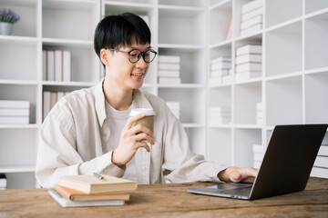 Fototapeta premium male student in casual clothes sitting at wooden table with laptop and writing notes while preparing for exam in library.