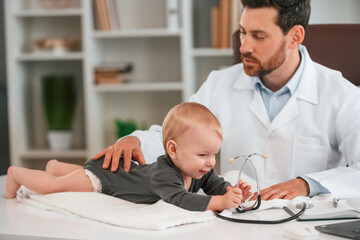 With stethoscope. Doctor with little baby is working in the cabinet