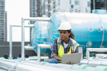 Female engineer worker using laptop computer inspecting quality sewer pipes at rooftop of building....