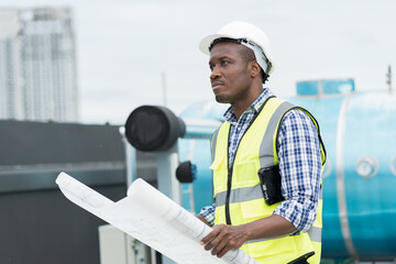 Male engineer worker working, holding blueprint and inspecting structure of building at rooftop of...