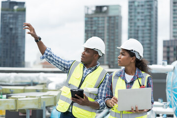 Male and female engineer worker working with laptop computer discuss and inspecting structure of building at rooftop of building at construction site