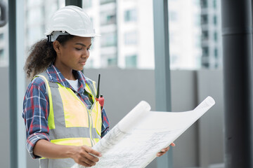 Female engineer worker working, holding blueprint and inspecting structure of building at rooftop of building at construction site