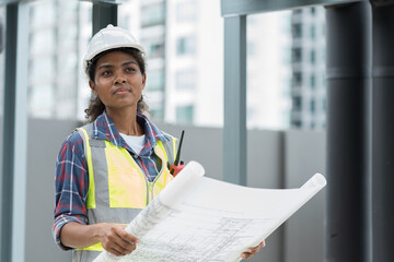 Female engineer worker working, holding blueprint and inspecting structure of building at rooftop of building at construction site