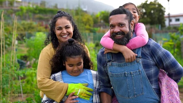 Happy indian family smiling in front of camera with organic garden in the background - Asian parents and children having fun together outdoor - Harvest and healthy lifestyle 