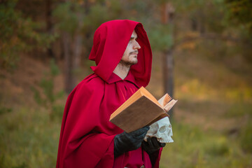 A sorcerer in red clothes with a skull and a book in his hands reads a spell. Medieval monk reads a...