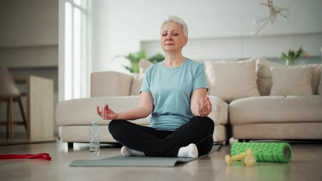 Happy mature woman exercising on floor at home. Attractive adult woman doing yoga stretching yoga online at home. Healthy lifestyle. Sport In Mature Age Concept.