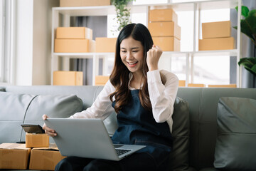 Happy young Asian woman entrepreneur, Smile for sales success after checking order from online shopping store in a laptop at home, Concept of merchant business online and eCommerce.