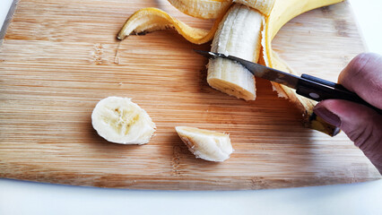 Banana with open panel and cutting with a knife of round pieces on wooden board and white background. Ripe banana with peel Close up and cooking. Delicious sweet fruit dessert