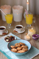 Plate of chocolate pralines, bowl of cookies, cups of tea, glasses of juice and lit candles on the table. Selective focus.