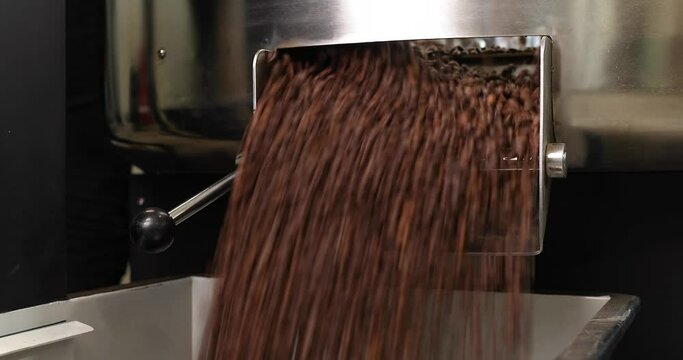 The coffee is roasted using high technology in a production machine. Lots of coffee in the vat. A man's hand in a black glove turns on the lever. Arabica and Robusta production concept.