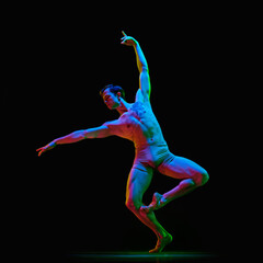 Portrait of young handsome, muscle men, ballet dancer in pastel color clothes posing over dark background with neon light. Contemporary, modern dance style