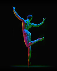 Portrait of graceful muscled male ballet dancer posing on one leg with spreaded hands up over dark studio background with neon light. Back view