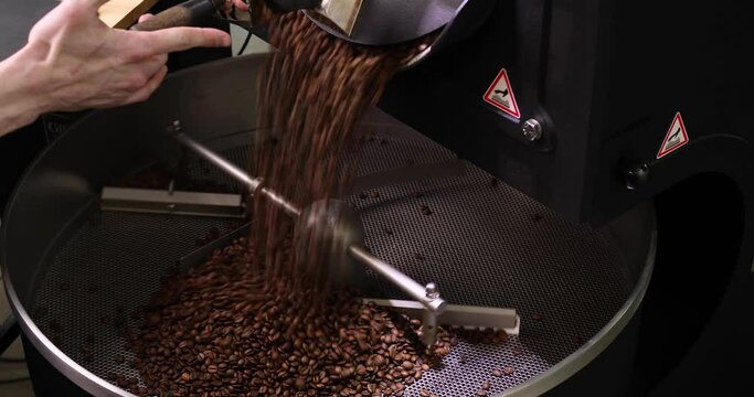 Large metal vat for roasting coffee beans close-up. The rotating mechanism stirs the coffee beans. Close-up of a hand turnning on the lever. The concept of industrial cooking arabica and robusta.