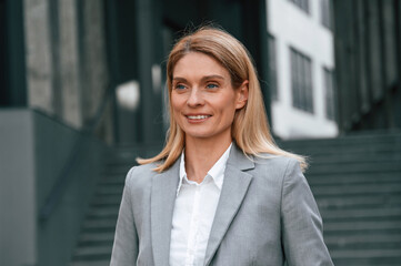 Woman in formal clothes is outdoors near the business building