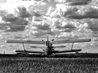 old double wing or biplane. in open grassy airfield. black and white finish. dynamic sky with white...