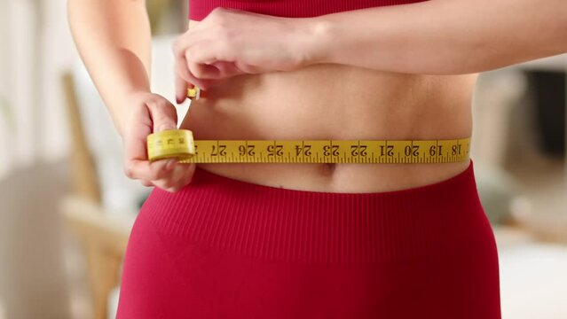 Sporty girl measuring hew waist line. Losing weight concept, dieting. Calorie control
