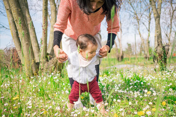 a mother helping her baby daughter move the first steps in a meadow in the countryside outdoors. Toddler making her first steps with mother teaching and helping. concept of growing up and family 
