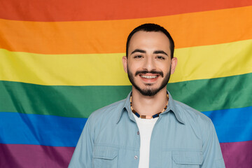 Cheerful gay man looking at camera near lgbt flag at background, International Day Against...