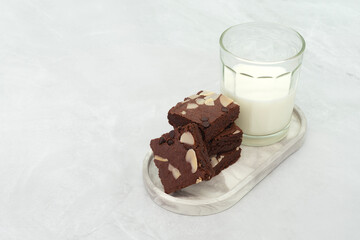 Brownies and milk glass on stone texture background. Chocolate brownie with sliced almond nuts toppings. Chocolate Brownie pieces. selective focus.