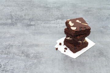 Brownies on paper on stone texture background. Chocolate brownie with sliced almond nuts toppings. Chocolate Brownie pieces. selective focus.