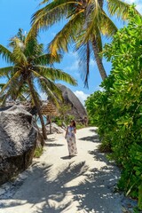 Girl wearing sun dress and hat walking on sandy beach with palm trees