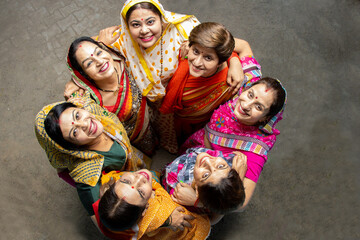 Group of happy young traditional indian women wearing colorful sari looking up and embracing each...