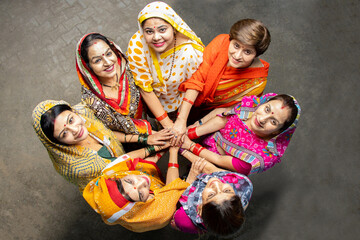 Group of happy young traditional indian women wearing colorful sari looking up while join hands with each other like a team. Rural india. women empowerment. World women's day, Top view