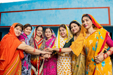 Group of happy young traditional indian women wearing colorful sari join hands with each other like...