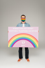gay man in medical mask with lgbt flag holding placard with International Day Against Homophobia,...