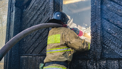 A firefighter extinguishes a fire through a window opening. Extinguishing a fire in a residential...