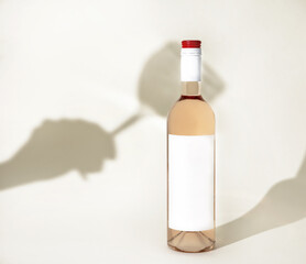 wine bottle with rose drink and white empty label isolated on beige with shadow on hand with glass in background.creative photo for winery factory advertising mockup free space for text
