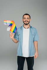 Smiling homosexual man holding lgbt flags and looking at camera isolated on grey.