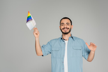 Bearded gay man in shirt smiling and holding rainbow lgbt flag isolated on grey.