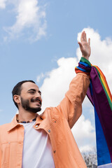 Cheerful gay man with lgbt flag waving hand on urban street, International day against homophobia.