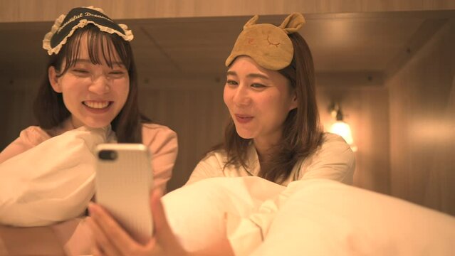 寝室でスマートフォンを使って遊んでいるパジャマ姿の女性たち
