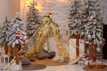 Tepee of luminous garlands against the backdrop of a brick wall and decorated Christmas trees © Svitlana