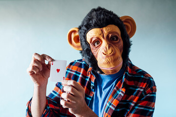 Man wearing monkey mask and holding poker playing cards on blue background. © karrastock
